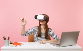 girl with virtual reality headset sitting at a desk with laptop and notebook