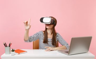 girl with virtual reality headset sitting at a desk with laptop and notebook