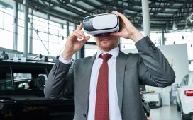 Man wearing classical suit standing at modern car showroom and using VR headset while testing new automobile