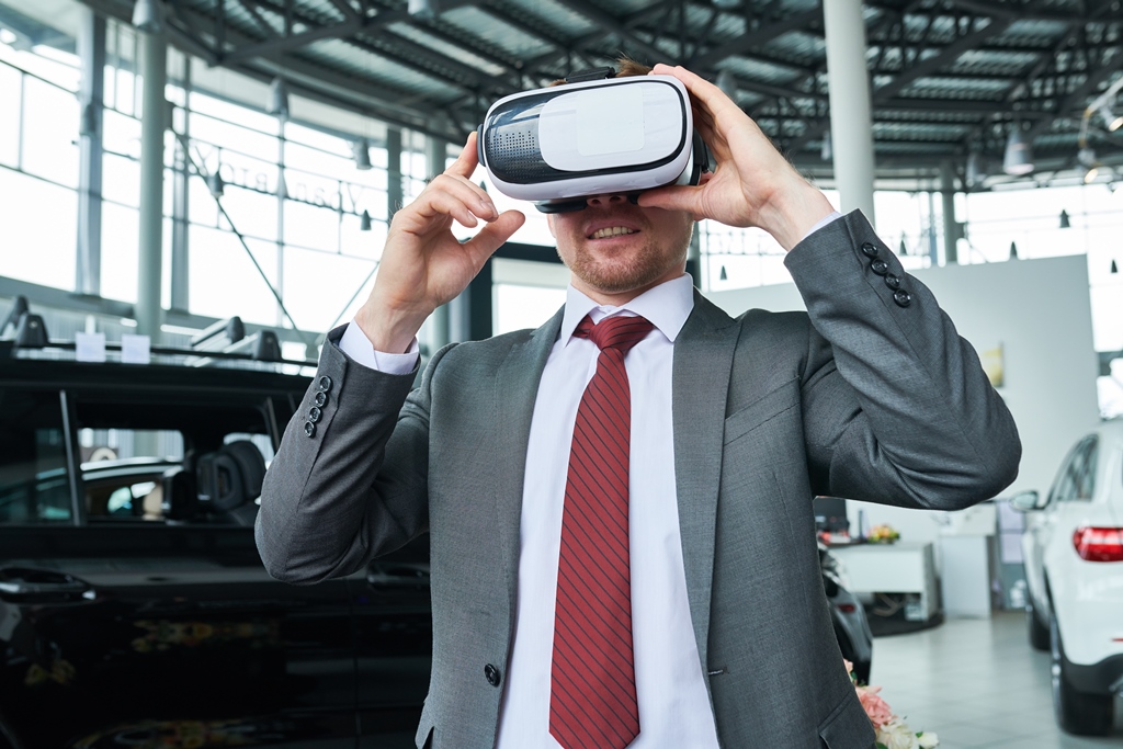Man wearing classical suit standing at modern car showroom and using VR headset while testing new automobile
