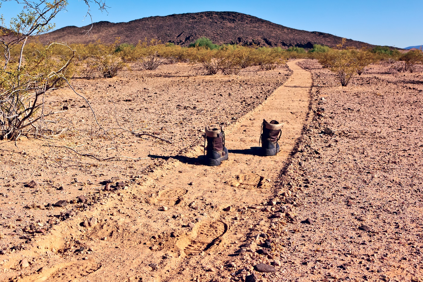 metaphorical depiction of undocumented immigrant - empty boots on a pathway through the desert